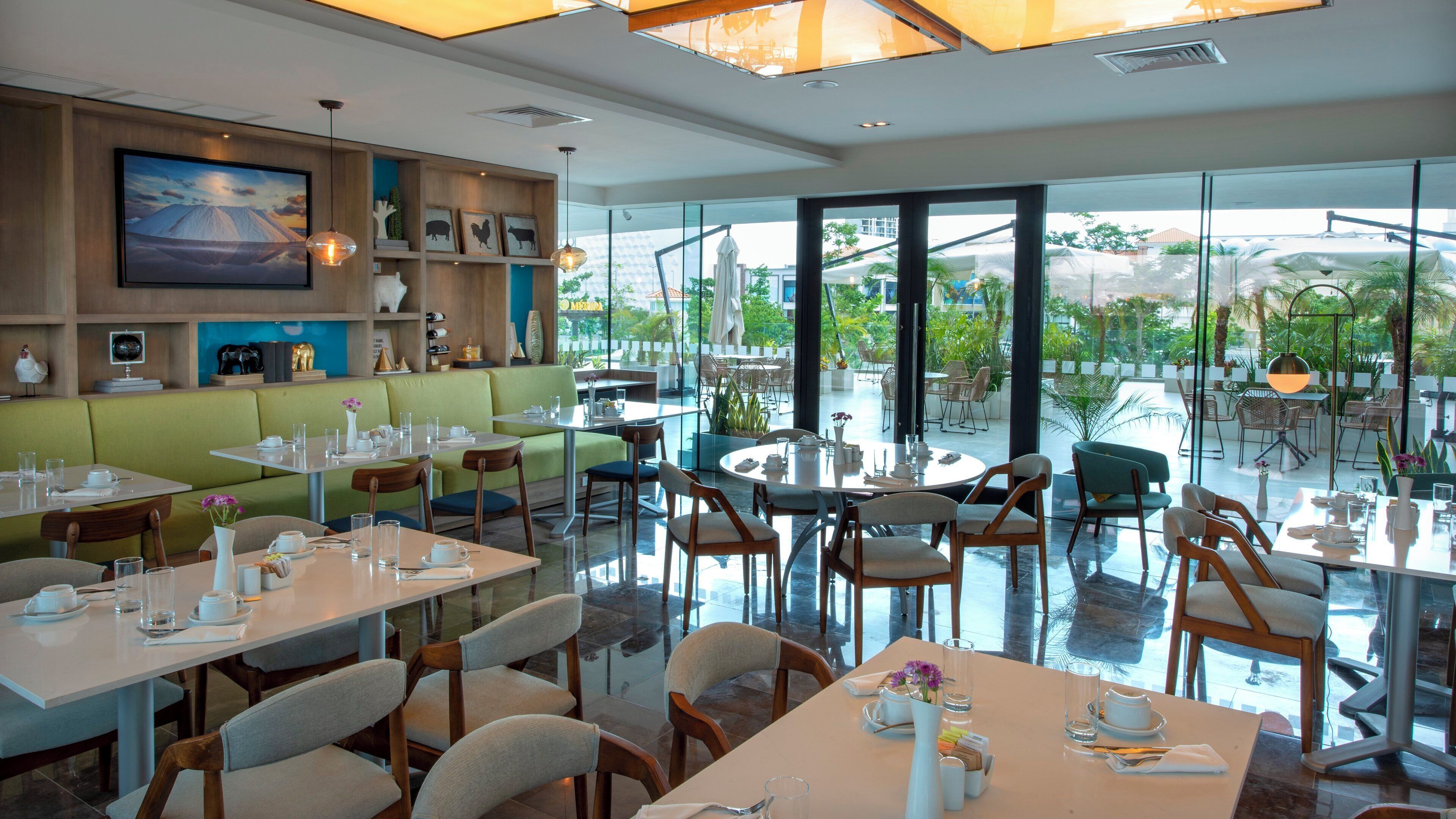 A restaurant with a modern interior, including a green booth seating area, round tables, and a view of the outdoors through large windows.
