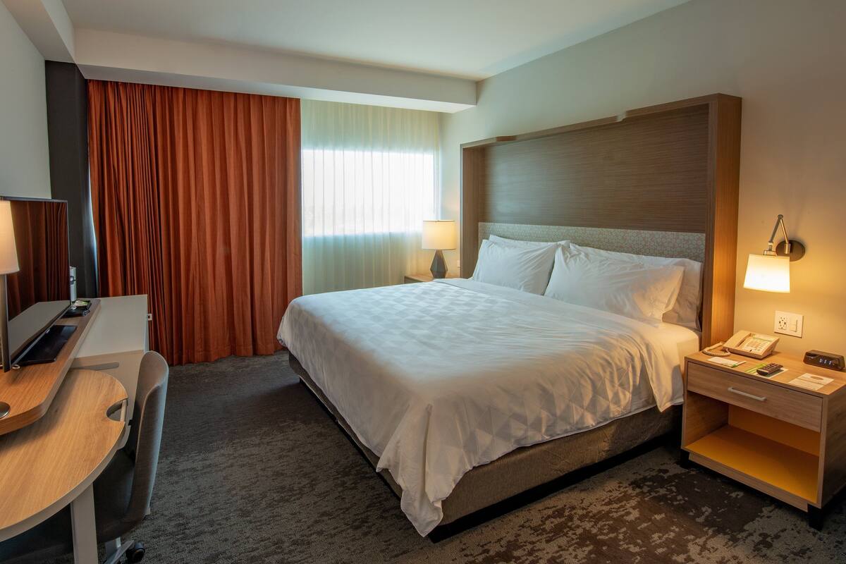 A hotel room with a bed, bedside table, lamp, desk, and a telephone.