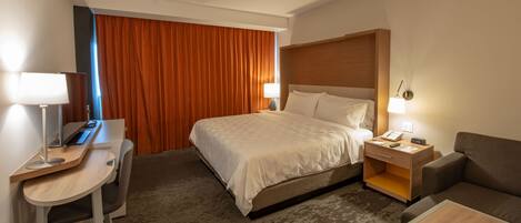 A hotel room with a bed, desk, chair, and a small sofa.