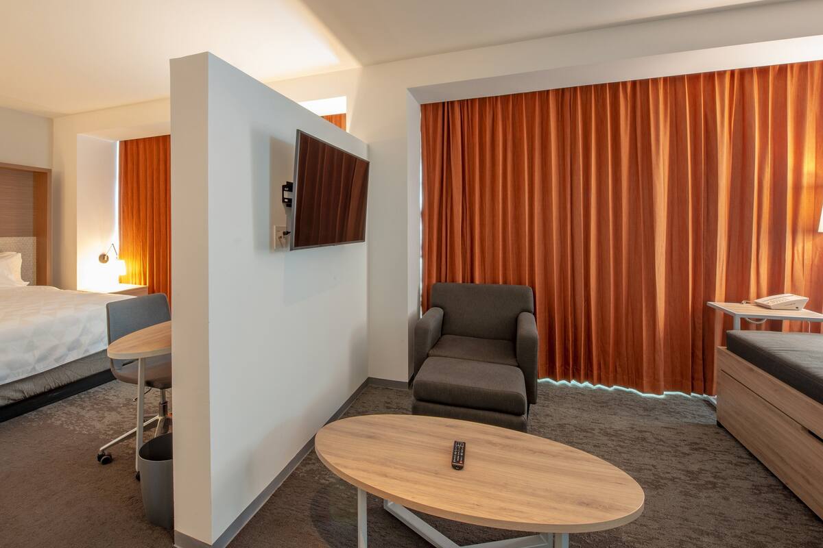 A hotel room with a bed, a desk, a chair, a TV, and a large window with curtains.