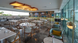Un restaurant spacieux, doté de nombreuses tables et chaises, d’un bar et de grandes fenêtres offrant une vue sur l’extérieur.