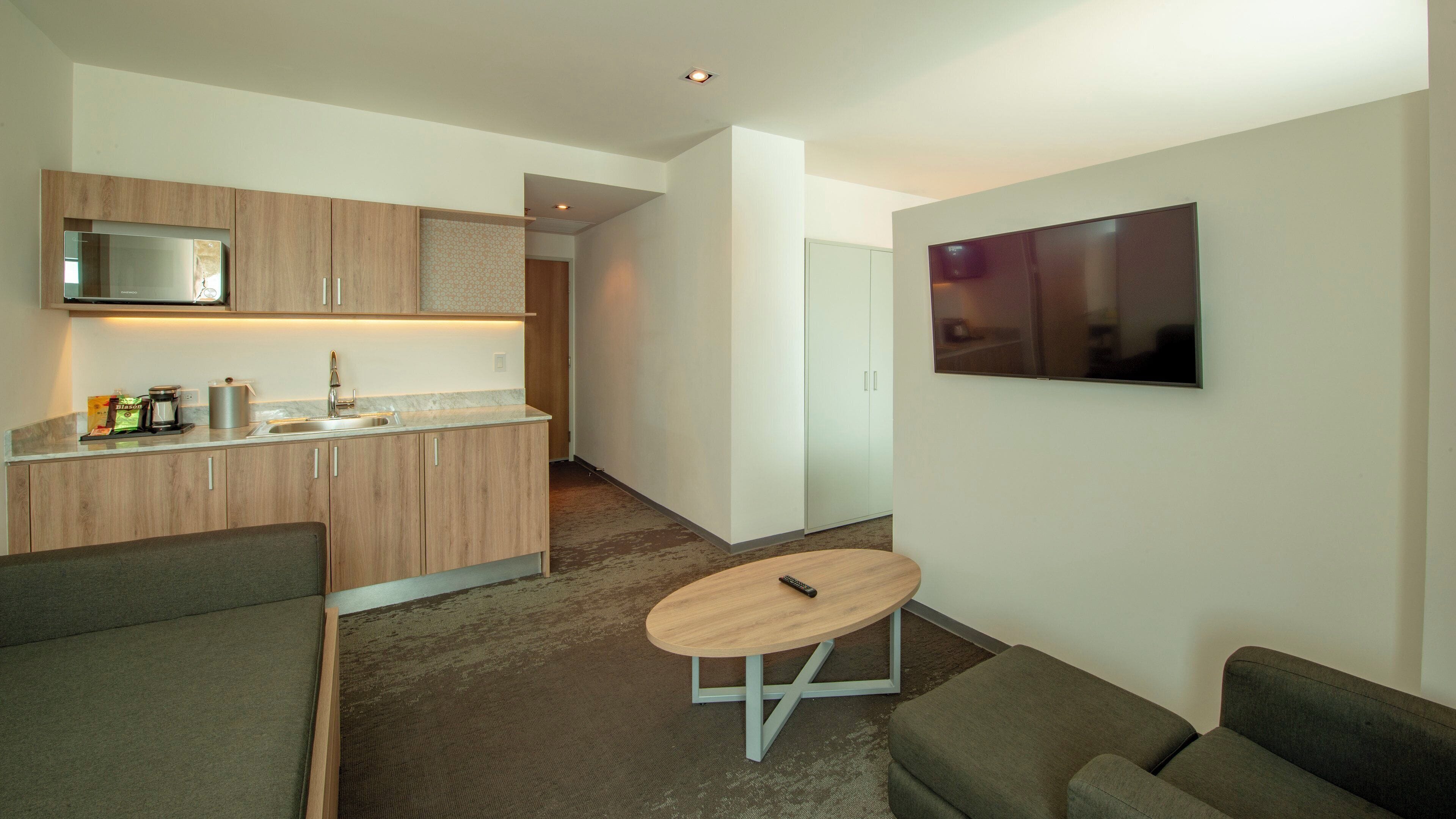 A compact living space with a kitchenette, a flat-screen TV, a sofa, and a small round table.