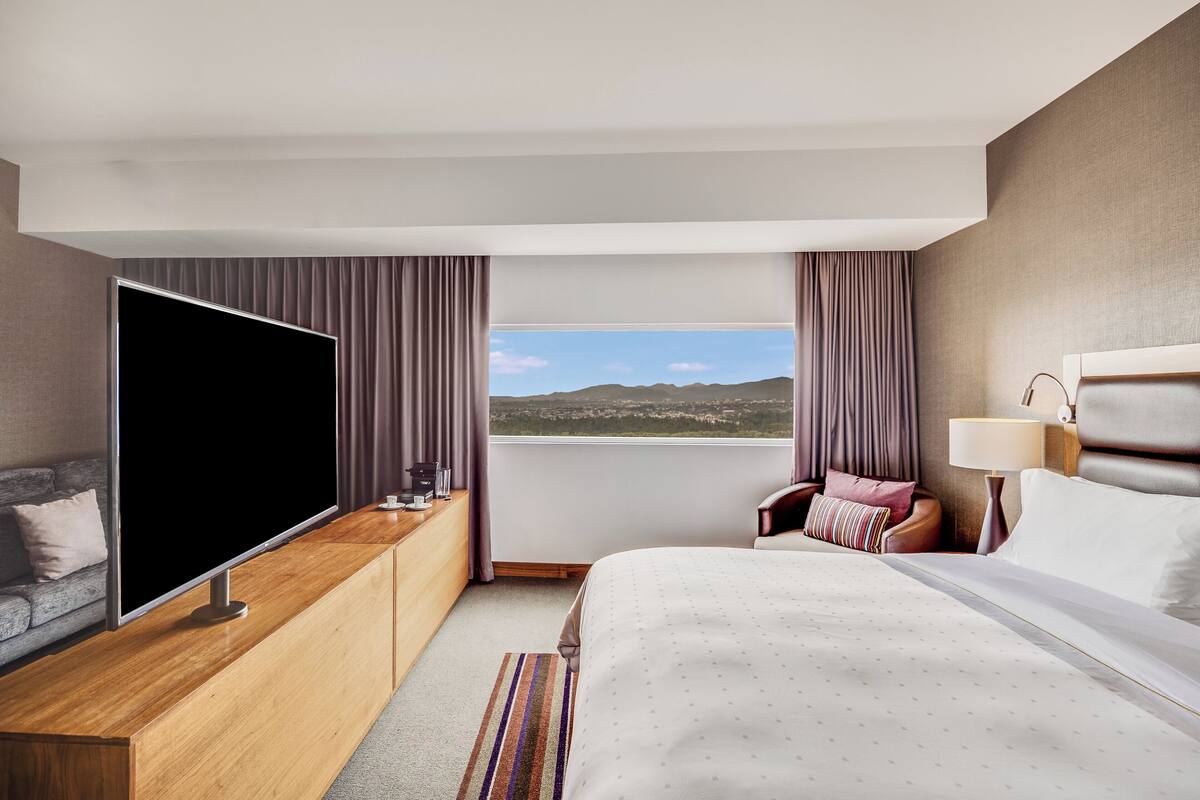 Une chambre d’hôtel moderne dotée d’un grand lit, d’une télévision à écran plat, d’un canapé et offrant une vue sur les montagnes.