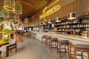 A modern bar area with wooden bar stools, hanging light fixtures, and a neon sign reading "Los Canarios".