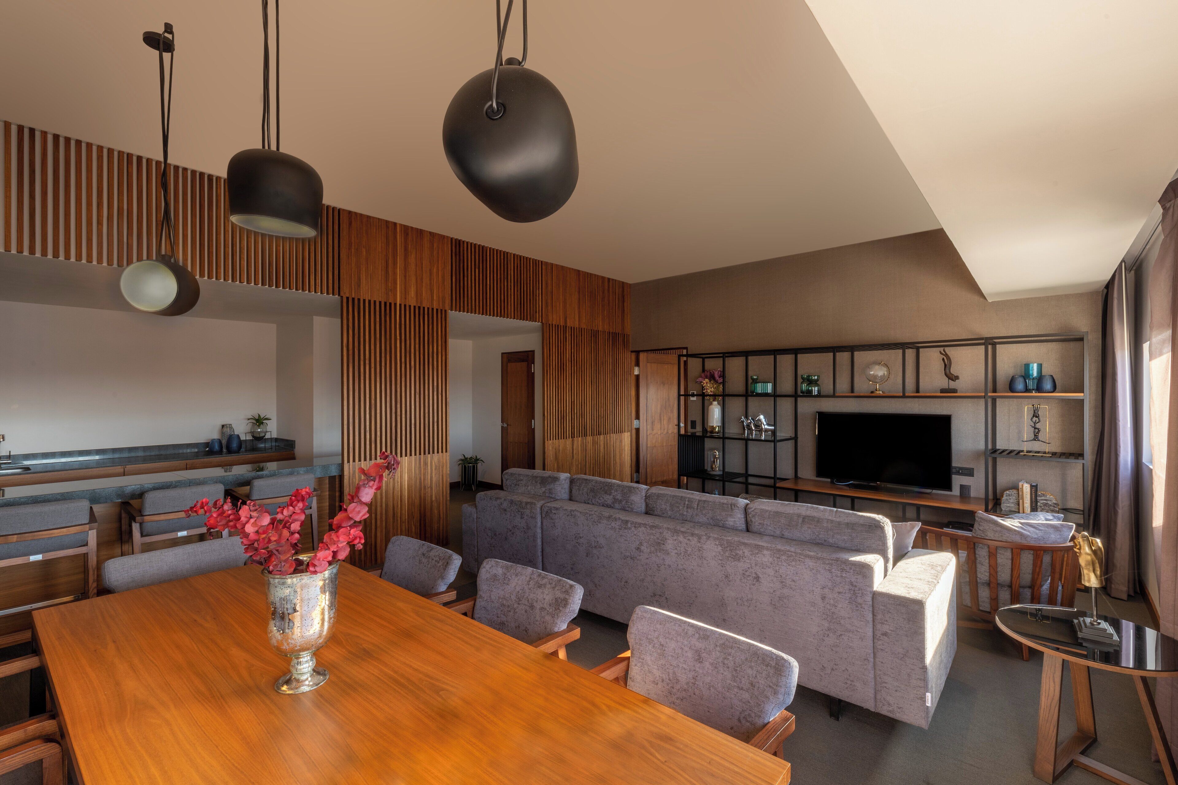 A modern living room with a wooden dining table, grey sofas, and a flat-screen TV.