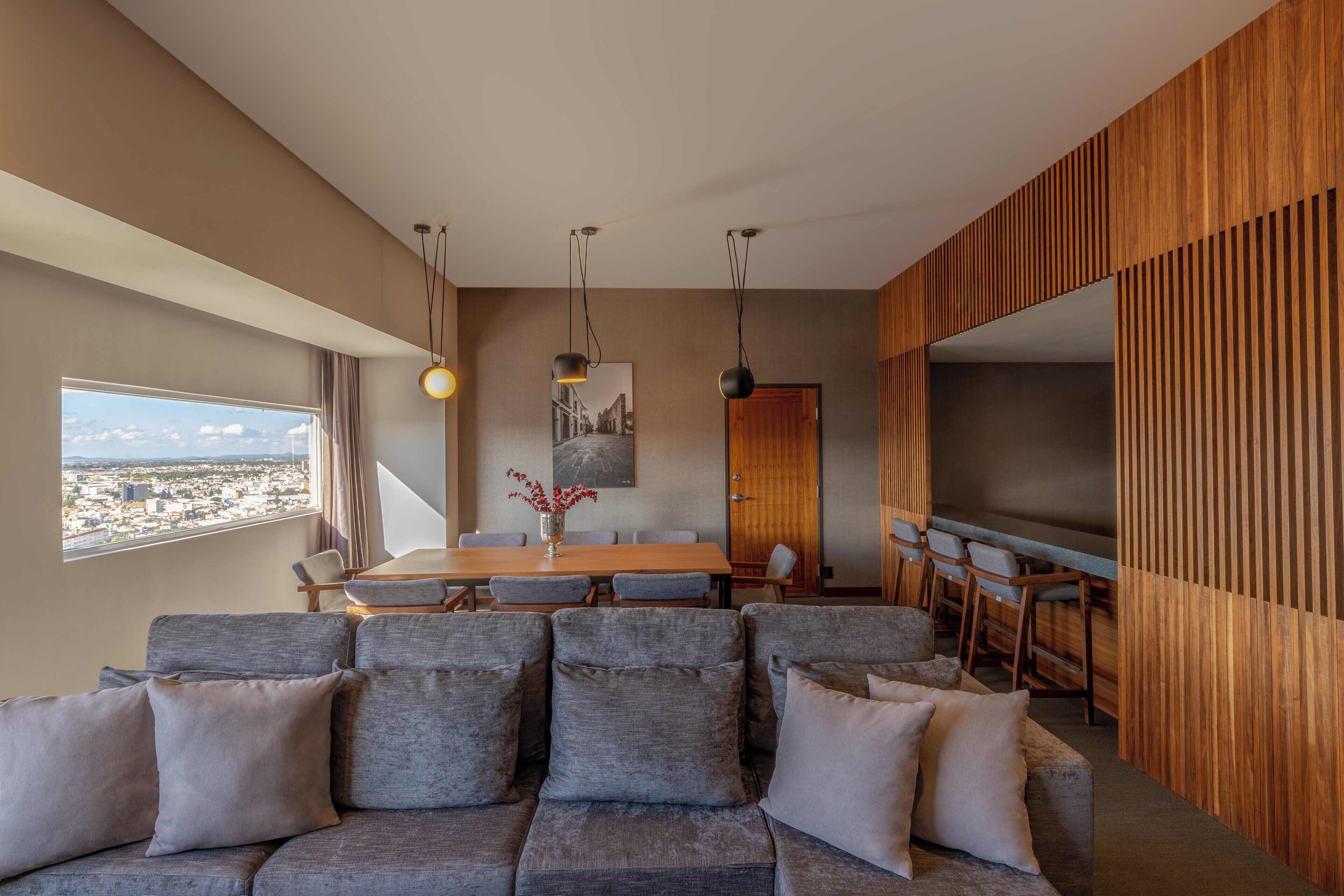 Un salon moderne avec un canapé gris, des murs recouverts de panneaux en bois, un coin repas avec une table et des chaises, et un grand téléviseur.