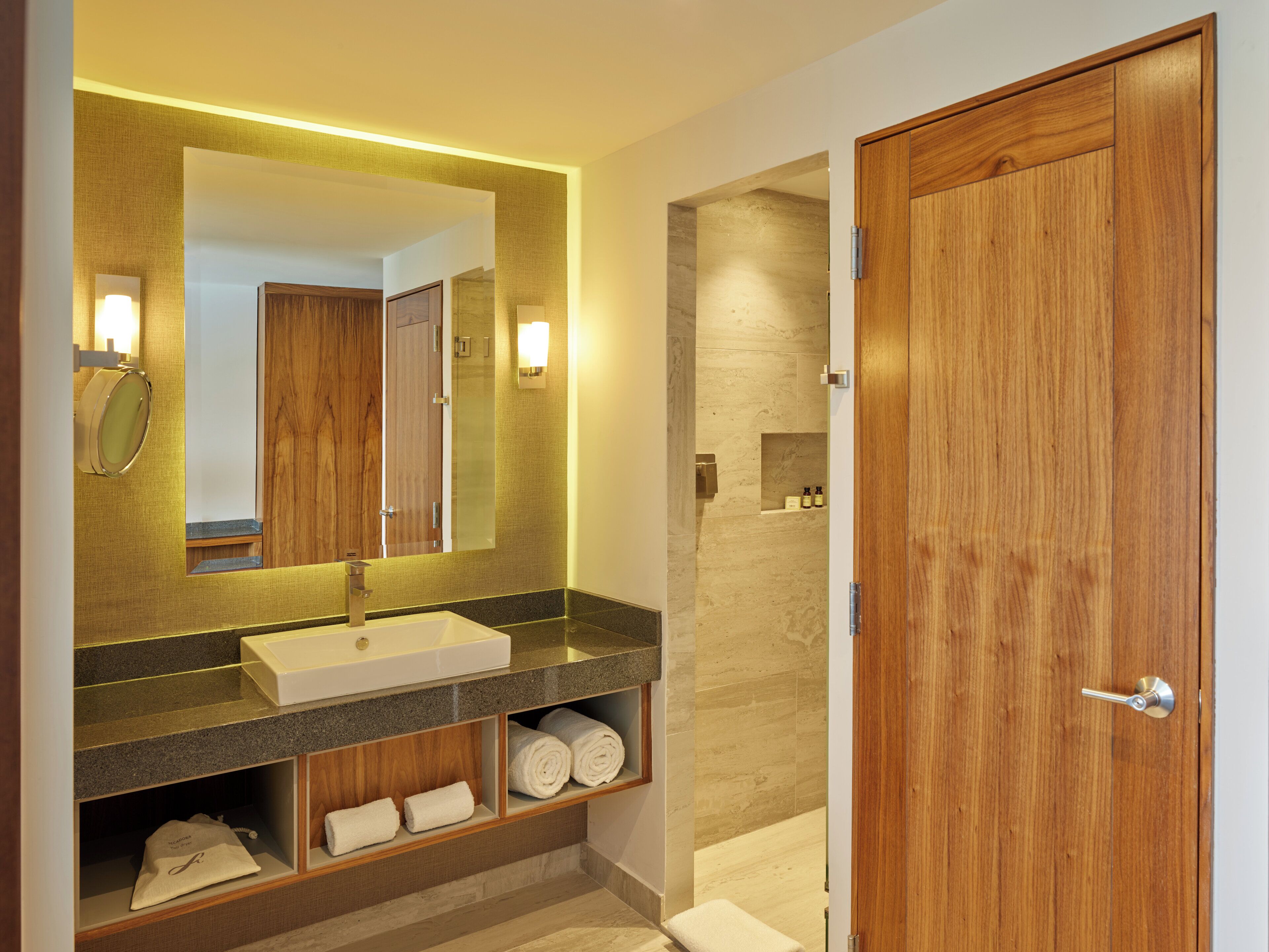 A modern bathroom with a large mirror, wooden vanity, and a shower area.