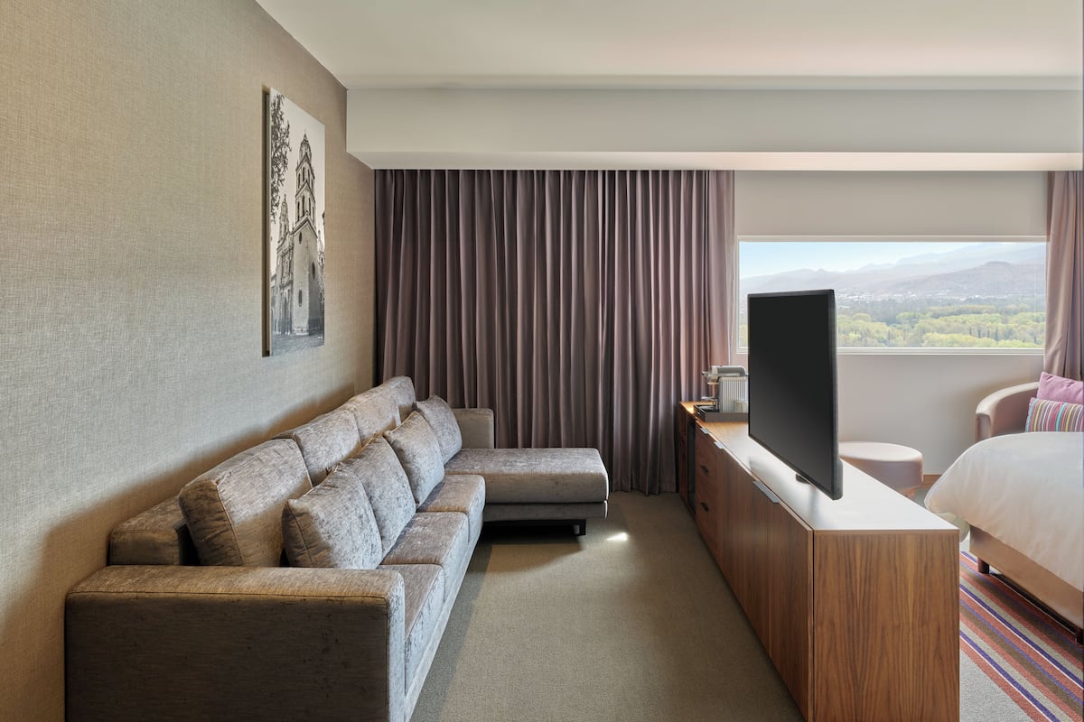 Une chambre d’hôtel moderne équipée d’un canapé, d’une télévision, d’un lit et offrant une vue sur les montagnes.