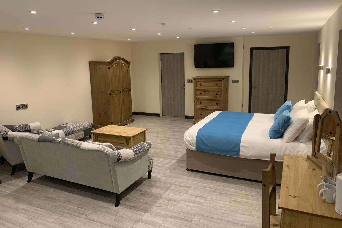 Una habitación de hotel moderna con cama, sofá, cómoda de madera y televisor en la pared.
