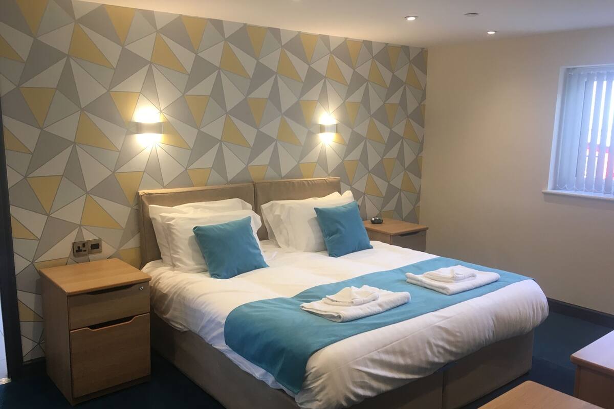 Una habitación de hotel moderna con una cama grande, dos mesitas de noche y una ventana con persianas.