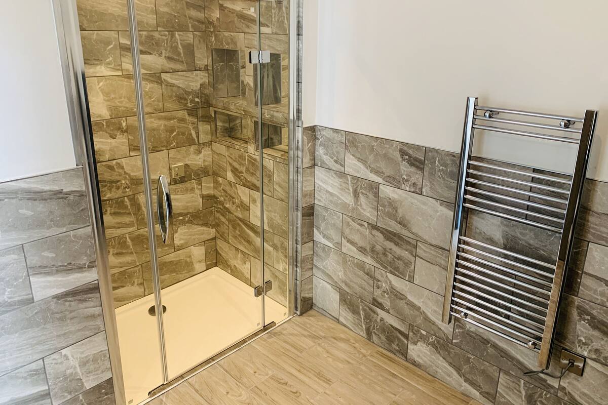 Un baño moderno con ducha de vidrio, baldosas de mármol y un toallero empotrado.