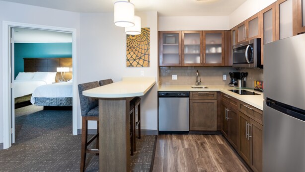 Cocina compacta con armarios de madera, lavavajillas, microondas y comedor con mesa y sillas.