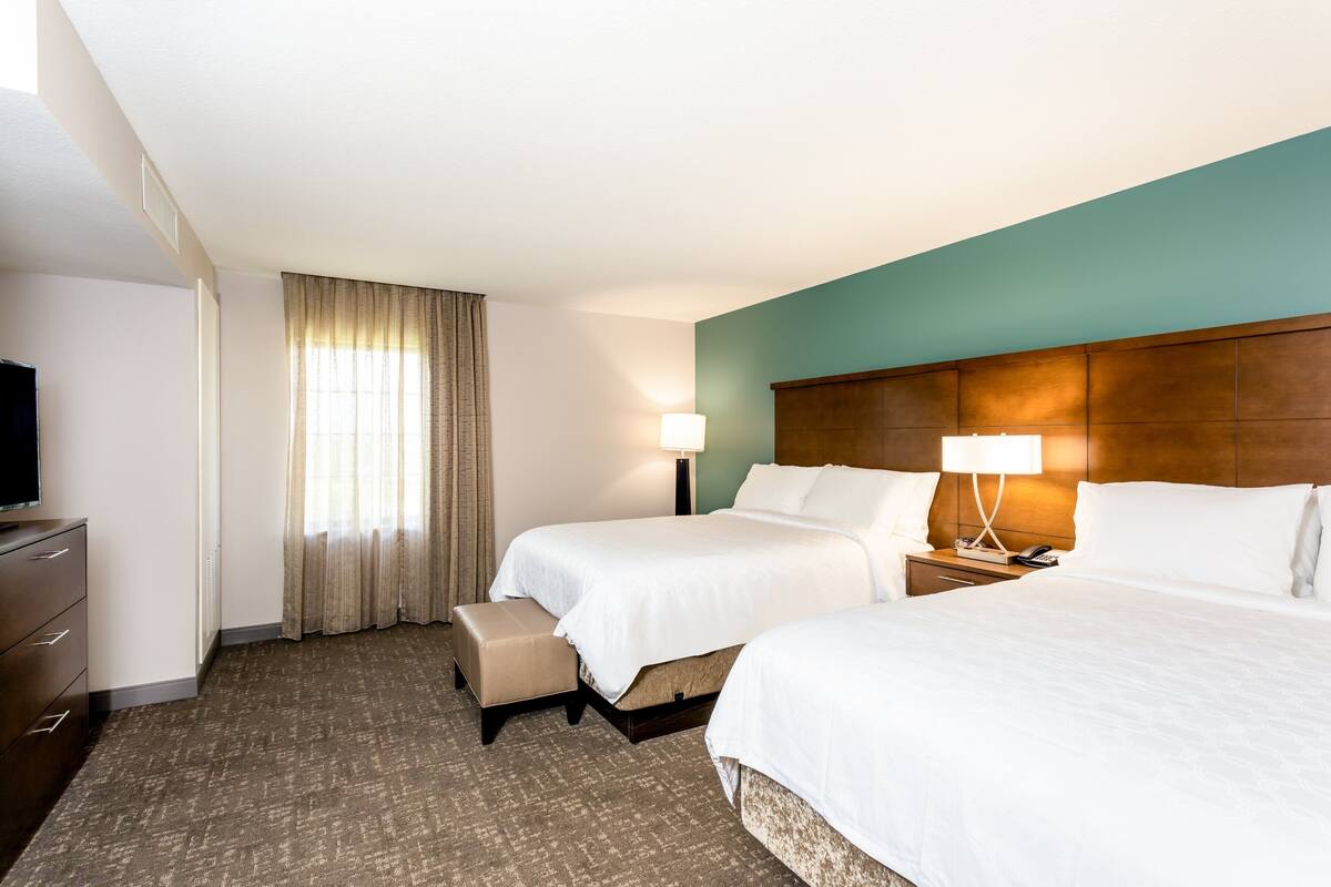 Habitación de hotel con dos camas, televisión, escritorio y ventana con cortinas.
