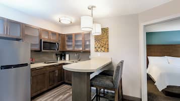 A compact hotel room with a kitchenette, a bed, and a seating area.