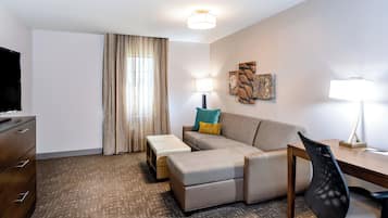 Habitación de hotel con televisor de pantalla plana, un sofá, una mesita, un escritorio y una silla.