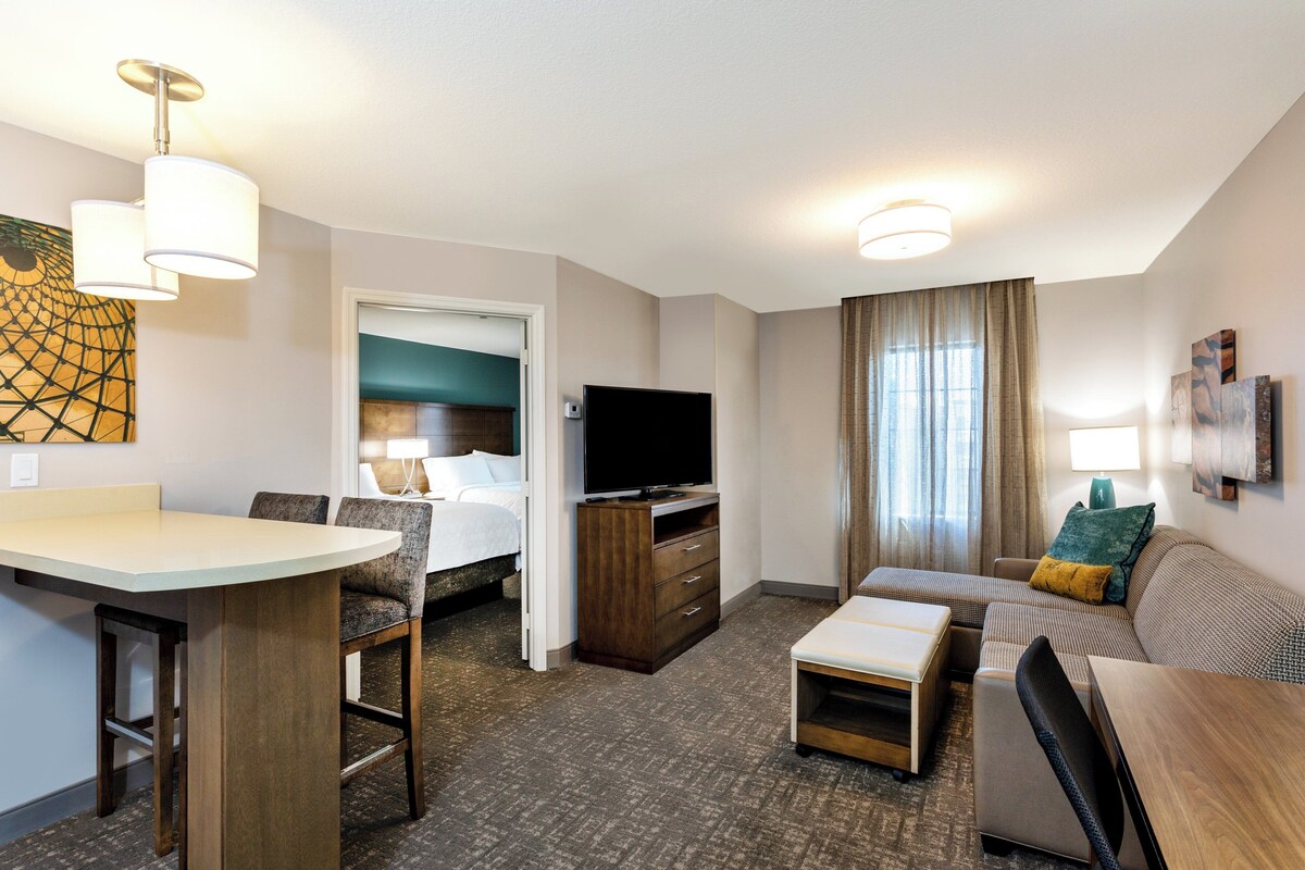Habitación de hotel con cama, televisor, zona de comedor, sofá y escritorio.