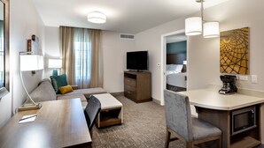 Habitación de hotel con sofá, escritorio y silla, televisor, cafetera y microondas.