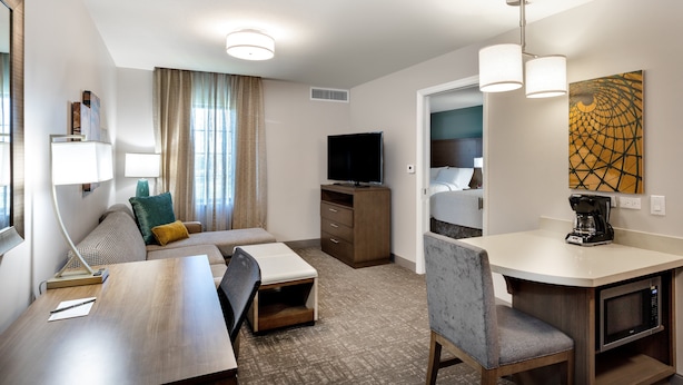 Une chambre d’hôtel équipée d’un canapé, d’un bureau avec une chaise, d’une télévision, d’une machine à café et d’un four à micro-ondes.