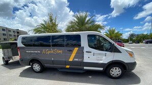 Una camioneta con la marca 'A Great Stay' y 'STAYBRIDGE SUITES ANING HOTEL', estacionada en un estacionamiento con otros vehículos y edificios al fondo.