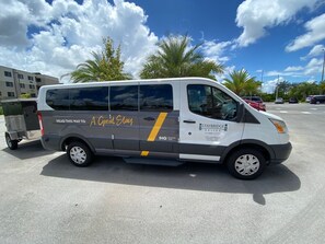 Una camioneta con la marca 'A Great Stay' y 'STAYBRIDGE SUITES ANING HOTEL', estacionada en un estacionamiento con otros vehículos y edificios al fondo.