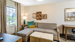 Ein Hotelzimmer mit Ecksofa, Schreibtisch aus Holz, einer Lampe und Bildern an der Wand.