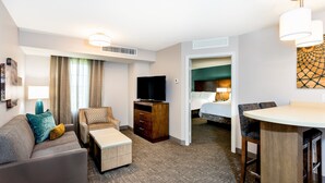 Habitación de hotel con sofá, una mesita, televisor, cama y zona de comedor.