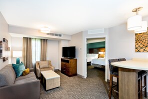 Habitación de hotel con sofá, una mesita, televisor, cama y zona de comedor.