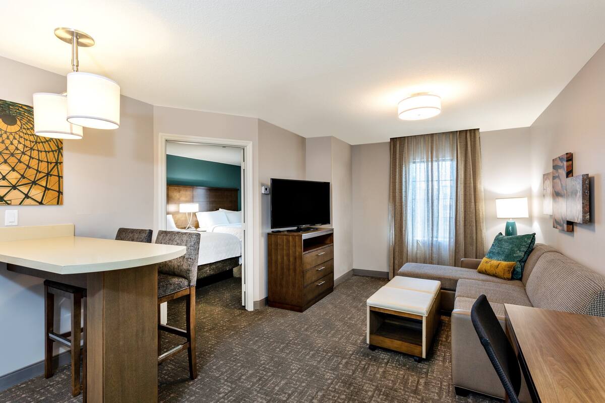 Habitación de hotel con cama, televisión, sofá, mesa de centro y escritorio con sillas.