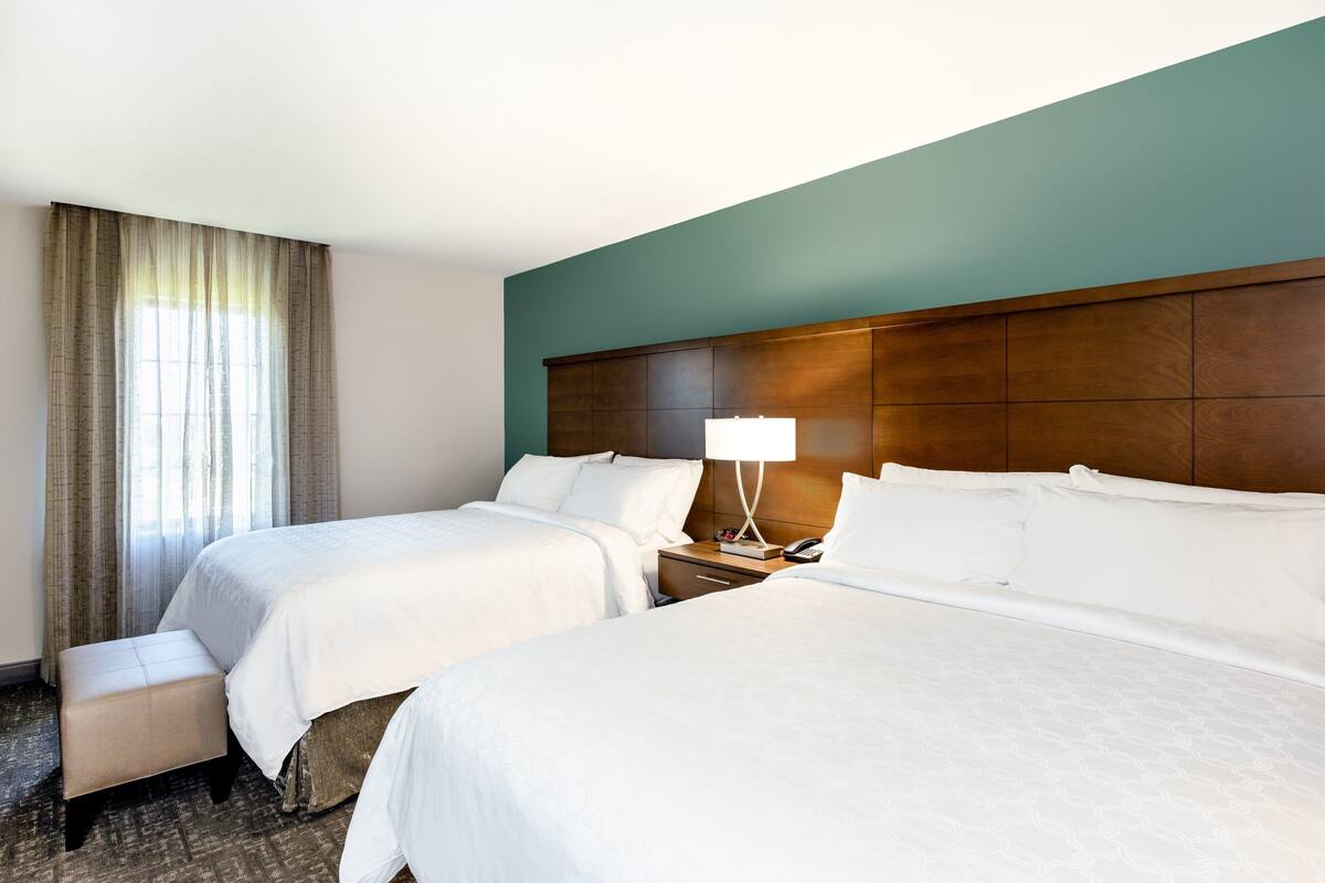 Habitación de hotel con dos camas, una mesita de noche con lámpara y una ventana con cortinas.