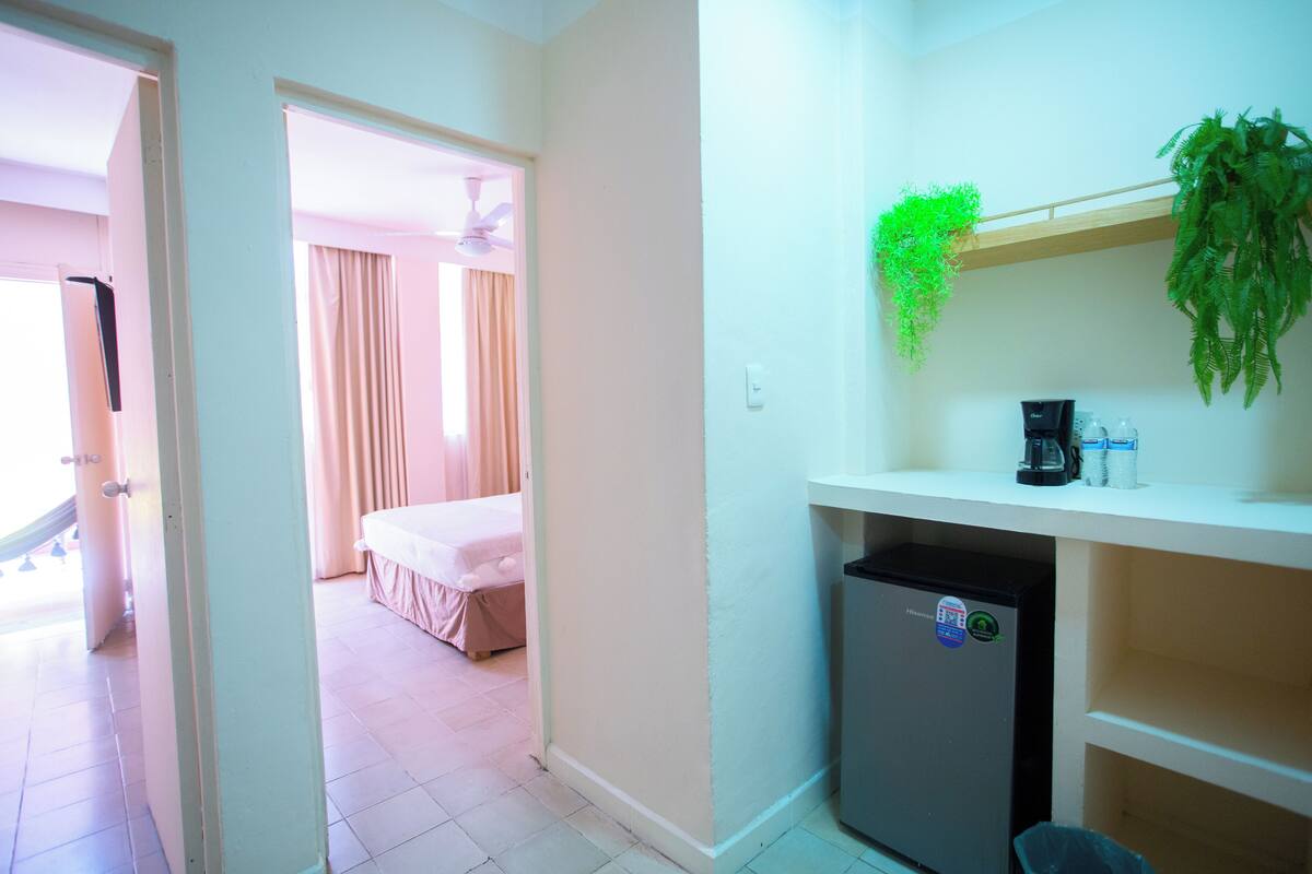 A compact hotel room with a kitchenette, a bed, and a bathroom visible through an open door.