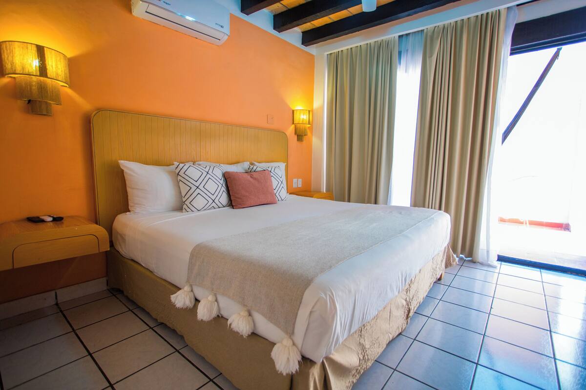 A hotel room with a large bed, two bedside lamps, a window with curtains, and a tiled floor.