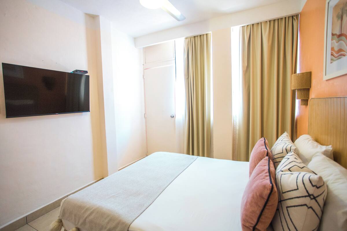 A hotel room with a bed, a television mounted on the wall, and a door leading to another room.