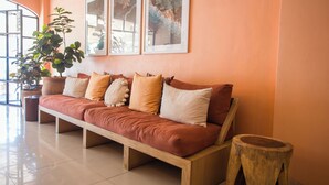 A modern living room with a wooden sofa, a large potted plant, and framed artwork on the wall. - Hotel Tropicus Boutique (Puerto Vallarta)