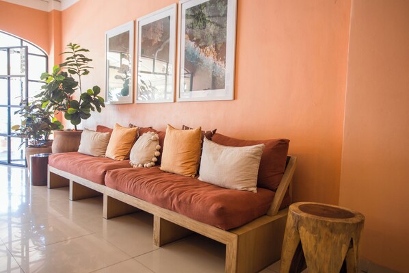 A modern living room with a wooden sofa, a large potted plant, and framed artwork on the wall. - Hotel Tropicus Boutique (Puerto Vallarta)