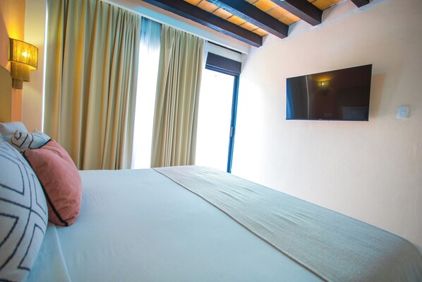 A hotel room with a bed, a TV mounted on the wall, and a window with curtains. - Hotel Tropicus Boutique (Puerto Vallarta)