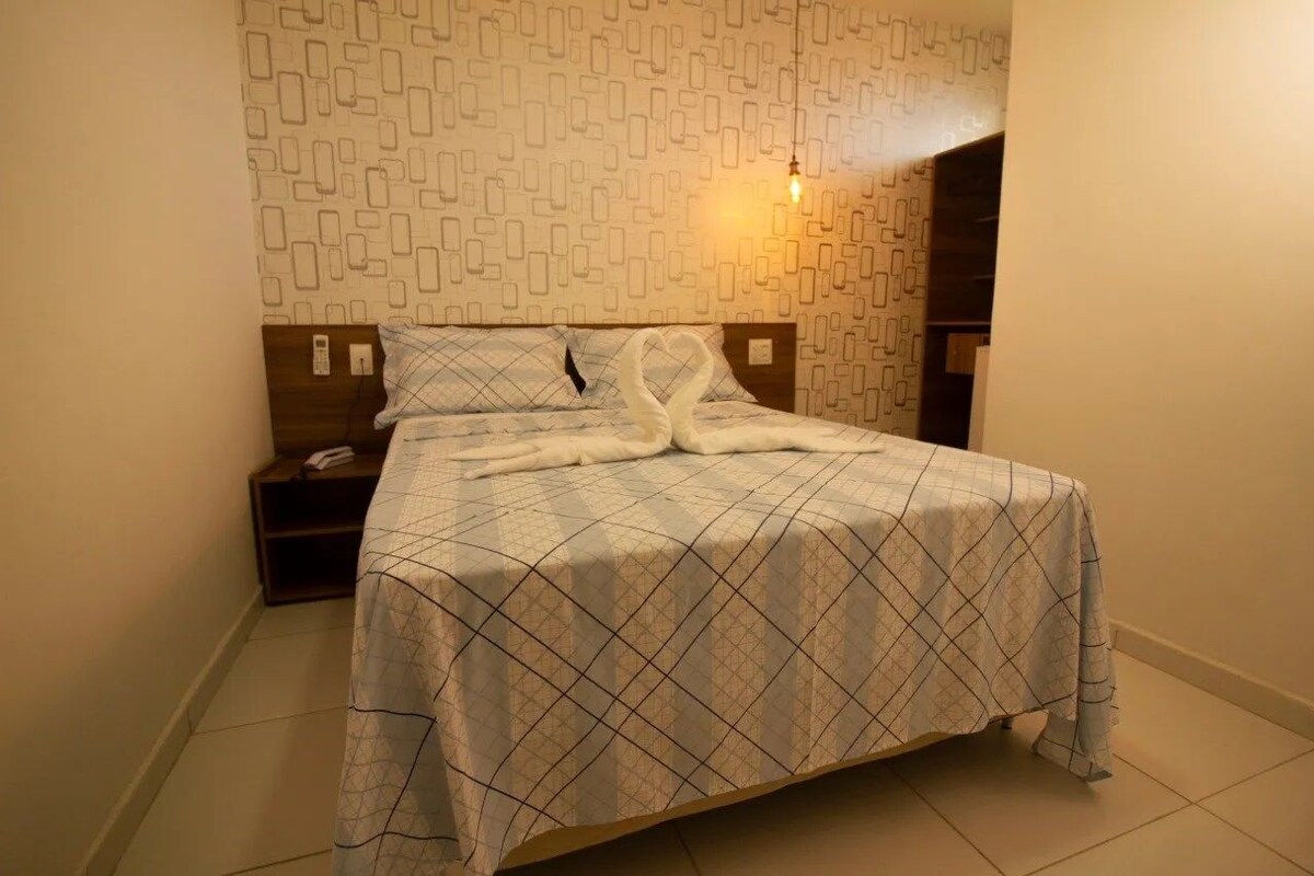 Un lit bien fait, recouvert d’une couvre-lit à motifs, une table de chevet avec une lampe et un mur décoré d’un motif.