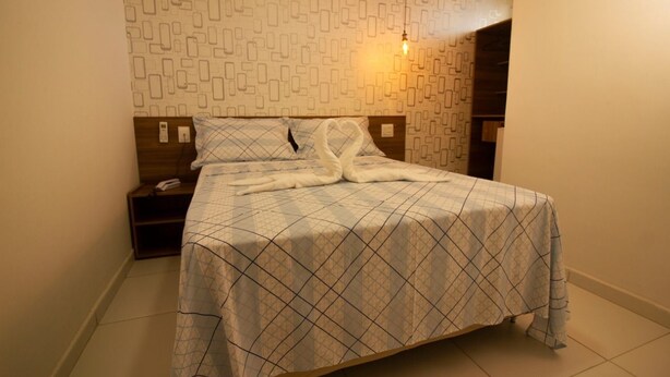 A neatly made bed with a patterned bedspread and two swan-shaped pillows. - Pousada Aliança (Ipojuca)
