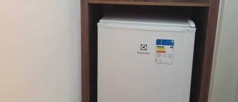 Un refrigerador pequeño y blanco en un pasillo estrecho, con estantes de madera arriba.