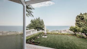 A view from a balcony overlooking a well-maintained lawn, a clear sky, and a distant body of water.