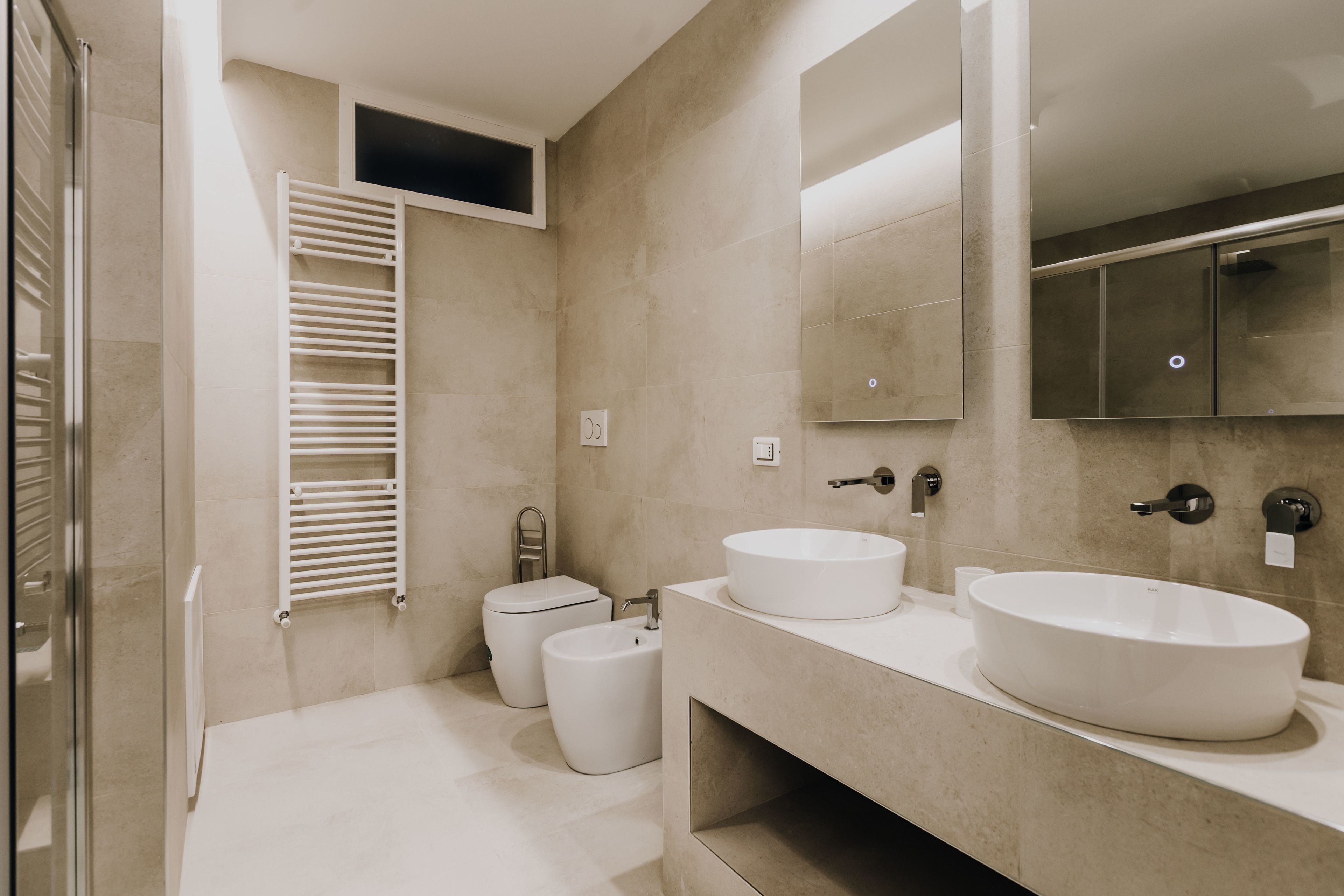 A modern bathroom with two sinks, a toilet, and a glass shower enclosure.