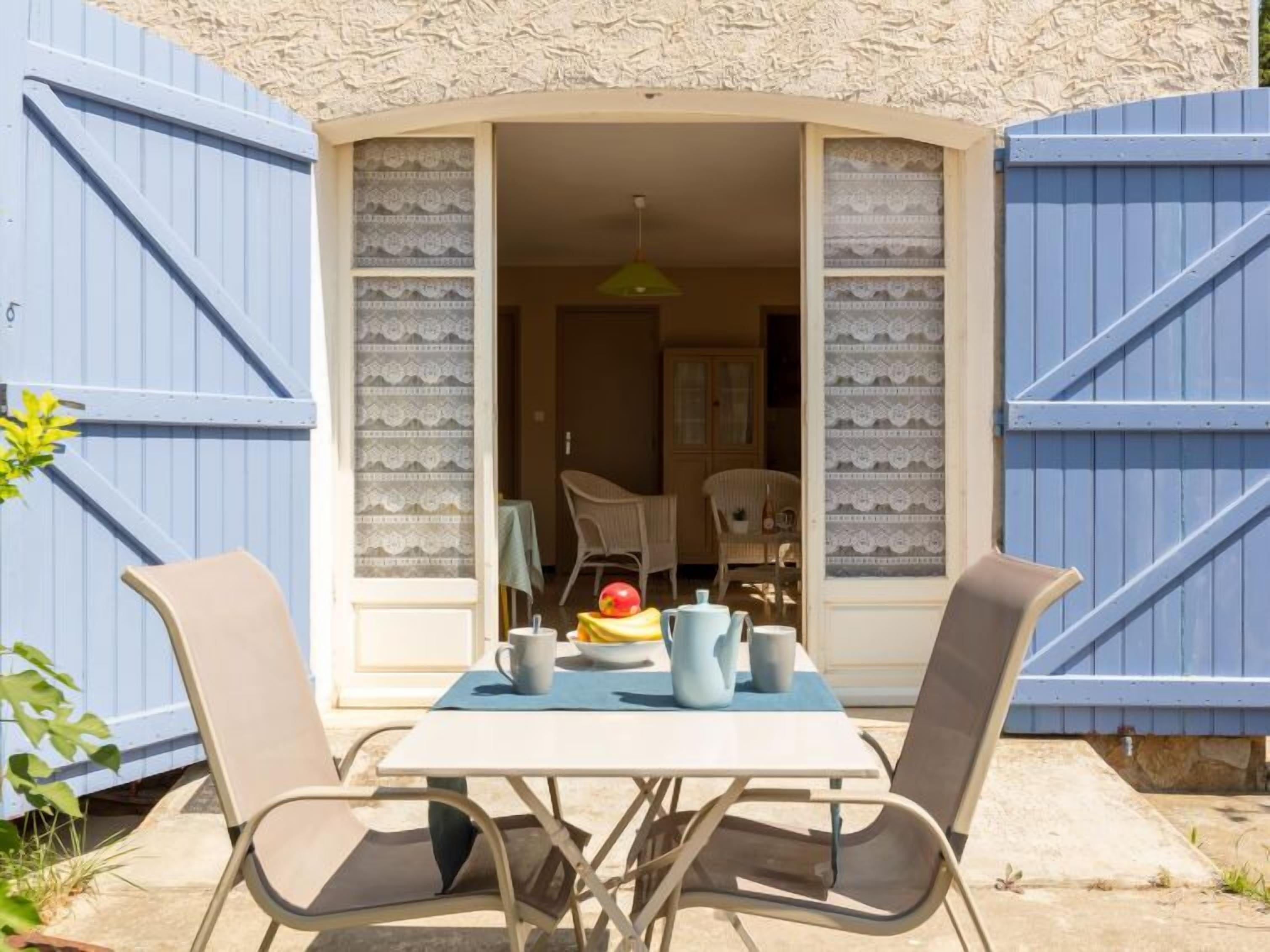 A patio with a table set for two, a chair, and a small plant.
