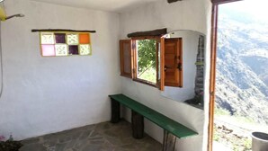 A small, rustic bathroom with a stone floor, a wooden bench, and a window with a view of a mountainous landscape. - Refugio Arrabales de la Alpujarra - Hostel (La Taha)