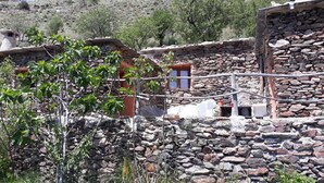 A rustic stone building with a small window and a door, surrounded by greenery and a hilly landscape. - Refugio Arrabales de la Alpujarra - Hostel (La Taha)