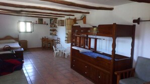 A rustic room with a wooden bed, a small table with chairs, and a window. - Refugio Arrabales de la Alpujarra - Hostel (La Taha)