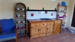 A kitchen with a wooden cabinet, a chair, and a shelf with kitchenware. - Refugio Arrabales de la Alpujarra - Hostel (La Taha)
