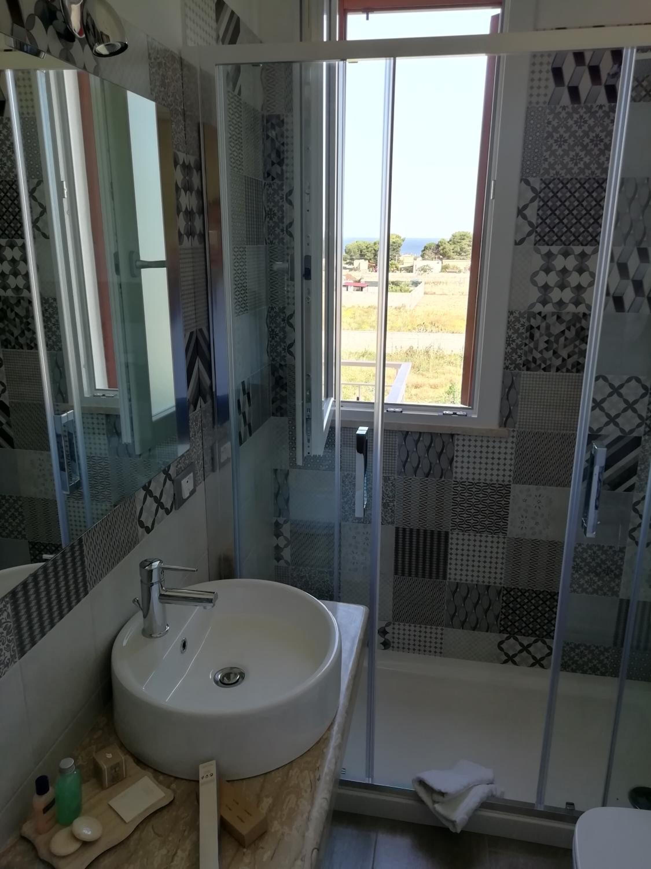 A bathroom with a large mirror, a sink, and a shower with patterned tiles.