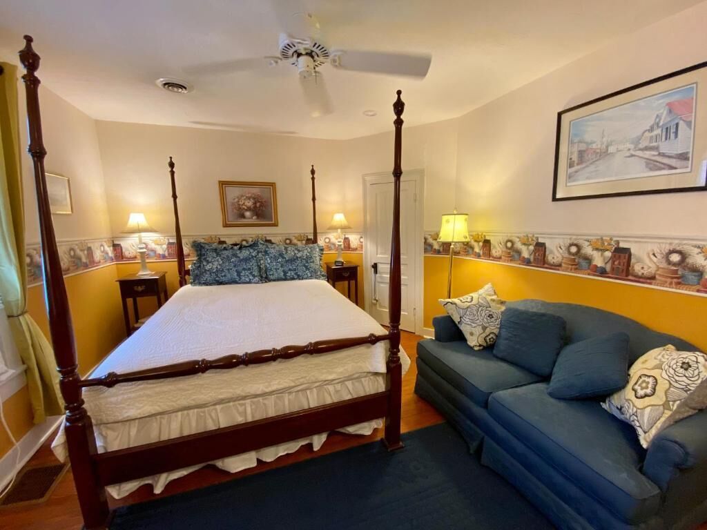 Un dormitorio con una cama con dosel, un sofá azul y un ventilador de techo.