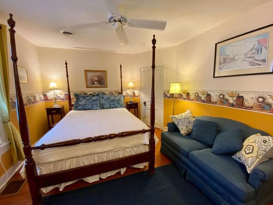 Un dormitorio con una cama con dosel, un sofá azul y un ventilador de techo.