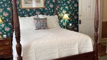 A four-poster bed with a white quilt, a floral wallpaper background, and a framed picture above it.