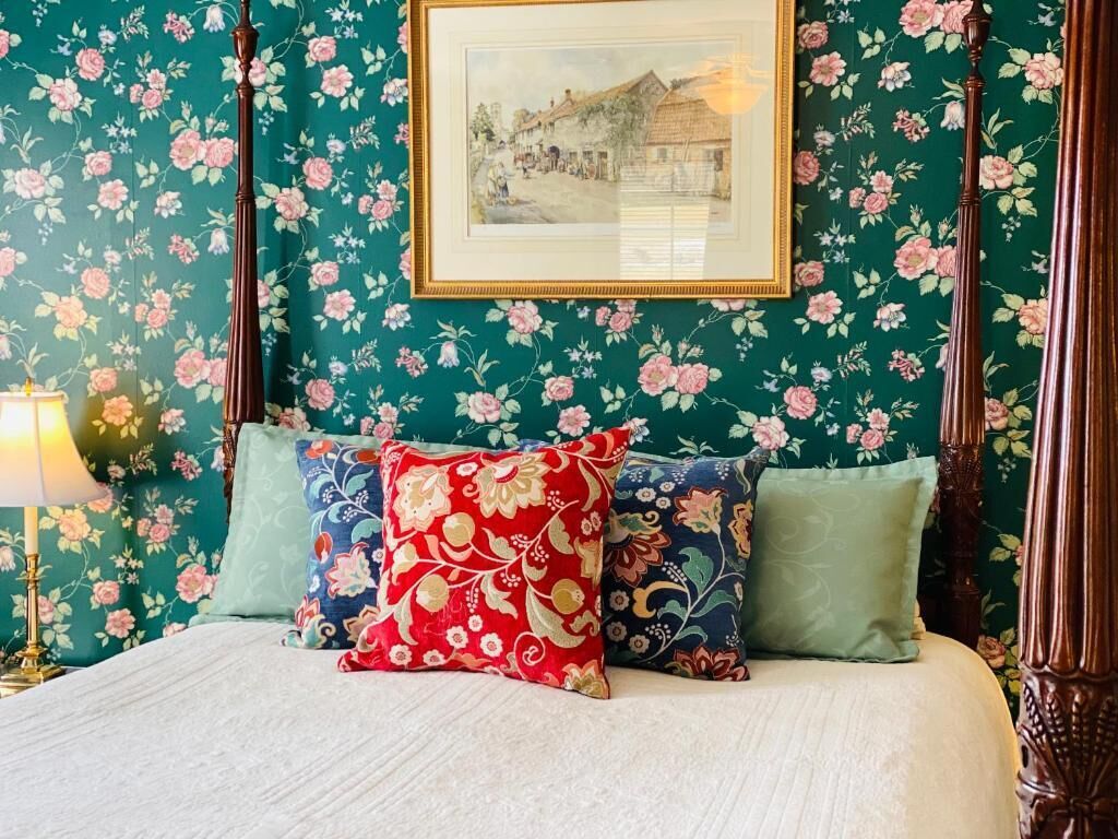 A bedroom with a four-poster bed, floral wallpaper, and a framed picture on the wall.